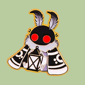 May include: A cartoon moth pin badge with a black body, red eyes, and feathery antennae. The moth has a white and black patterned cape and holds a lantern. The pin is set against a light green background.