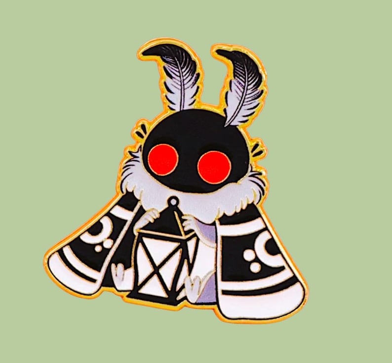 May include: A cartoon moth pin badge with a black body, red eyes, and feathery antennae. The moth has a white and black patterned cape and holds a lantern. The pin is set against a light green background.