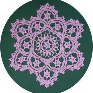 May include: A delicate, lacy doily in a soft pink color, with a starburst design. The doily is crocheted and has a circular shape.