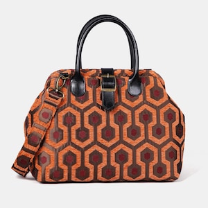 Peut inclure: Sac à main orange et marron à motifs géométriques, avec des poignées et des détails en cuir noir. Il est doté d'une bandoulière amovible et d'une fermeture à boucle.