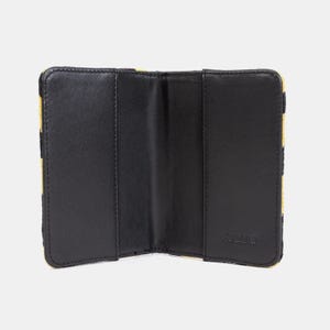 Peut inclure: Portefeuille en cuir noir avec un motif &agrave; carreaux jaune et noir &agrave; l'ext&eacute;rieur. Le portefeuille est ouvert et montre l'int&eacute;rieur avec trois compartiments. Le nom de la marque "Joanna" est imprim&eacute; &agrave; l'int&eacute;rieur.