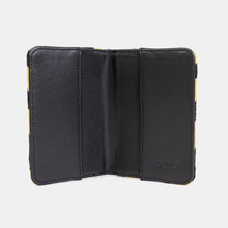 Peut inclure: Portefeuille en cuir noir avec un motif &agrave; carreaux jaune et noir &agrave; l'ext&eacute;rieur. Le portefeuille est ouvert et montre l'int&eacute;rieur avec trois compartiments. Le nom de la marque "Joanna" est imprim&eacute; &agrave; l'int&eacute;rieur.