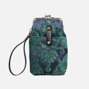 Puede incluir: Un pequeño bolso de mano con estampado verde y azul, cierre de latón y correa de cuero negro.