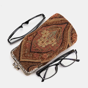 May include: An overhead shot of a brown patterned glasses case with a metal clasp, and two pairs of black-framed eyeglasses. The case has a detailed, woven design in shades of brown, orange, and gold. One pair of glasses is open, and the other is closed.