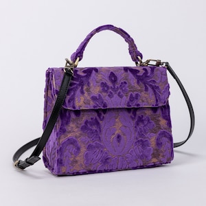 Bolso de mano artesanal con asa superior, bandolera con solapa frontal y terciopelo morado.