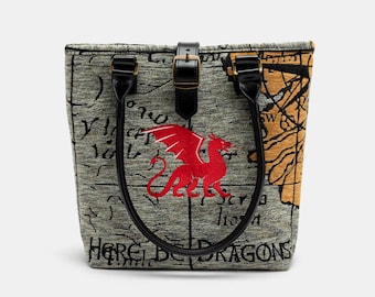 May include: A gray canvas tote bag with black leather straps and a red embroidered dragon. The bag has the text "Here Be Dragons" printed on the front.