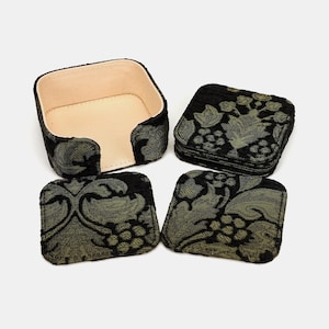 May include: A set of square coasters featuring a black and olive green floral damask pattern, accompanied by a matching square holder with a light beige interior. The coasters are made of fabric and the holder has a structured, open-front design.