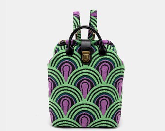 May include: A green and purple patterned backpack with black straps and a black leather handle. The backpack has a brass clasp.