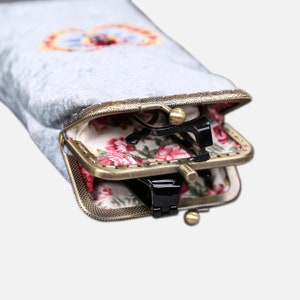 Op de afbeelding: Een grijs fluwelen brilletje met een voering met bloemenprint en een messing sluiting. De etui is open en er zitten twee brillen in.