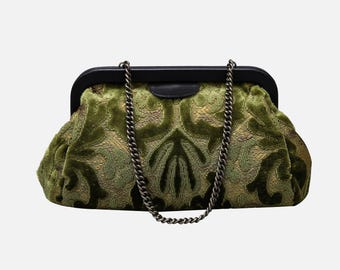 May include: A green velvet clutch bag with a black frame and a chain strap. The bag has a floral pattern.