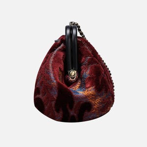 May include: A small, red velvet clutch bag with a gold chain strap and a black clasp. The bag has a quilted design and a floral pattern.
