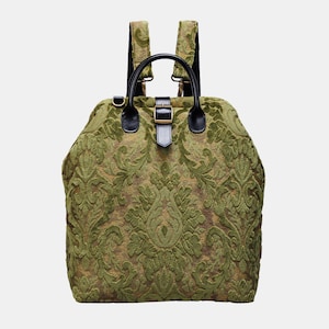 May include: A green velvet backpack with a black leather strap and buckle. The backpack has a damask pattern.
