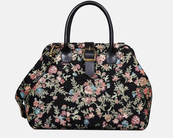 May include: Black handbag with a floral tapestry design. The bag features a top handle, a detachable shoulder strap, and a buckle closure. The floral pattern includes pink, blue, and green flowers on a black background. The bag has black leather accents.