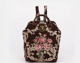 May include: A brown floral patterned backpack with a top flap closure and a brass buckle. The backpack has adjustable straps and a top handle.