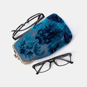 May include: Two pairs of black spectacles and a teal velvet glasses case with a floral pattern. The case has a metal clasp and frame. One pair of glasses is open, and the other is closed.