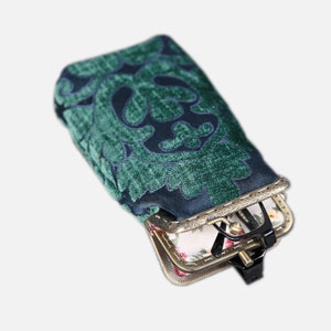 Puede incluir: Una bolsa de terciopelo verde con un patrón floral y un cierre de metal dorado. La bolsa está abierta y hay un par de gafas dentro.