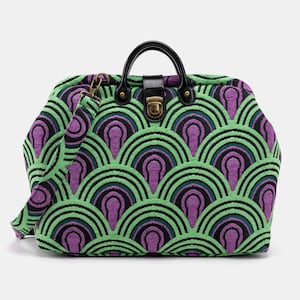 May include: A green and purple patterned travel bag with a black leather handle and a brass lock. The bag has a shoulder strap.