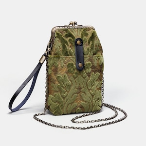 May include: A small green velvet purse with a chain strap and a black leather flap. The purse has a floral pattern and a brass clasp.