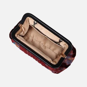 May include: A red velvet clutch with a black frame and a quilted design. The inside of the clutch is lined with a beige fabric.