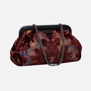 May include: A burgundy velvet clutch bag with a chain strap. The bag has a floral pattern in shades of blue and orange.