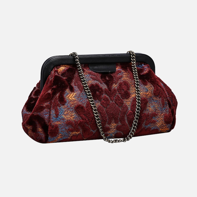 May include: A burgundy velvet clutch bag with a chain strap. The bag has a floral pattern in shades of blue and orange.