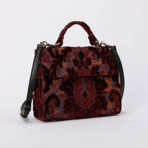 Bolso de mano artesanal con asa superior, bandolera con solapa frontal y bandolera de terciopelo color vino.
