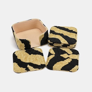 May include: A set of four square coasters and a matching holder. The coasters and holder are covered in a black and tan zebra stripe pattern. The holder has a light tan interior.