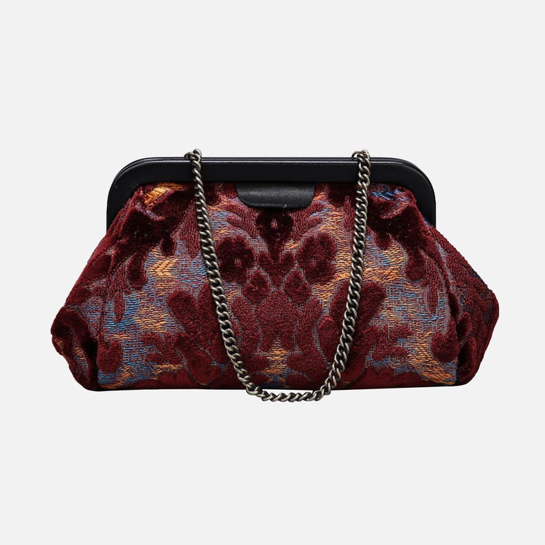 May include: A burgundy velvet clutch with a chain strap and a floral pattern. The clutch has a black frame and a gold-toned chain.
