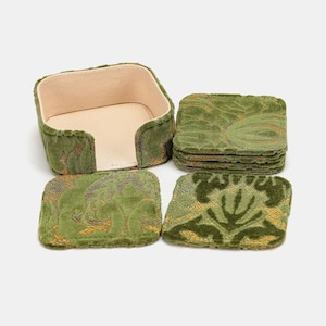 May include: A set of four square coasters and a matching holder. The coasters and holder are covered in a green and gold floral patterned fabric. The holder has a beige interior.