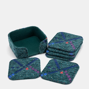 May include: A set of square coasters and a matching holder. The coasters and holder are teal with a textured pattern and a geometric design in blue, red, and purple. The holder is square with a teal interior.