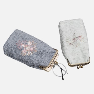 May include: Two fabric eyeglass cases with floral embroidery. One case is gray with a pink floral design and the other is light green with a white floral design. Both cases have a gold metal clasp.