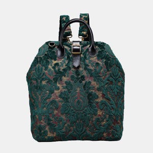 Puede incluir: Una mochila de terciopelo verde con un patrón de damasco dorado y burdeos. La mochila tiene una hebilla de cuero negro y correas ajustables.