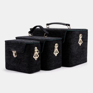 May include: Three black fabric storage cases with brass-toned clasps and handles. The boxes are rectangular with rounded lids and a textured finish. The smallest case has a clasp, the others have decorative latches. Green trim.
