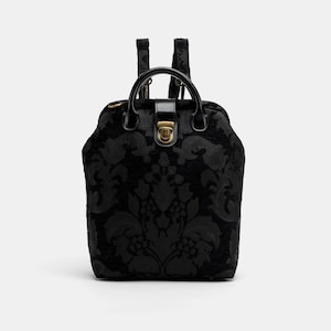May include: Black backpack with a damask pattern and a gold-toned clasp. The backpack has a top handle and adjustable straps.
