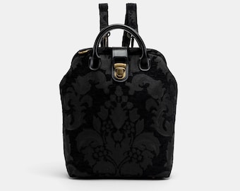 May include: Black backpack with a damask pattern and a gold-toned clasp. The backpack has a top handle and adjustable straps.