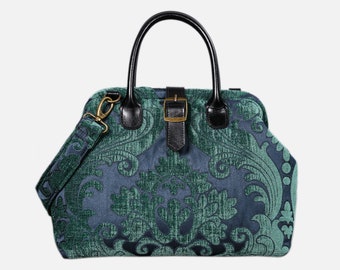 May include: A teal blue and green patterned handbag with a black leather handle and strap. The bag has a gold buckle and a detachable shoulder strap.