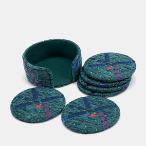 May include: A set of six teal fabric coasters with a matching holder. Each coaster features a geometric design in blue, red, and purple. The holder and coasters are made of a textured fabric.