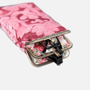 May include: A pink floral patterned glasses case with a gold metal frame and a floral patterned lining. The case is open and a pair of black glasses is inside.