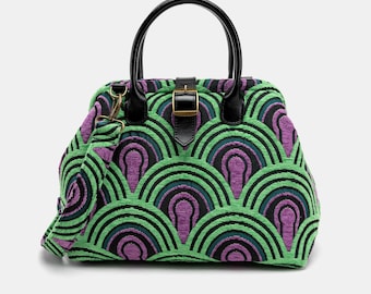 May include: A patterned handbag featuring a repeating geometric design in green, purple, and black. The bag has a black handle, a detachable shoulder strap, and a buckle closure. The bag is a satchel style.