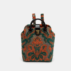 Puede incluir: Una mochila pequeña de color verde y naranja con estampado, con correas negras y un asa negra. La mochila tiene un cierre dorado.