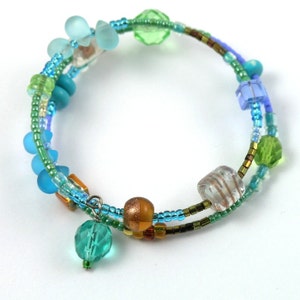 May include: A multi-strand bracelet with blue, green, and brown beads. The bracelet is made of glass beads and has a charm hanging from it.