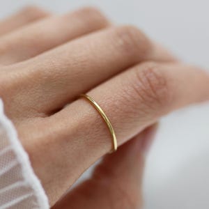 Könnte beinhalten: Ein dünner, goldfarbener Ring wird an einem Finger getragen. Der Ring hat ein schlichtes, minimalistisches Design und scheint aus Metall zu sein. Der Ring ist ein zarter Schmuck.