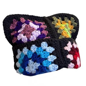 May include: A headband constructed from multiple crocheted granny squares joined with black yarn. The squares feature vibrant floral-inspired patterns in shades of purple, lavender, yellow, green, blue, light blue, pink, and deep red.