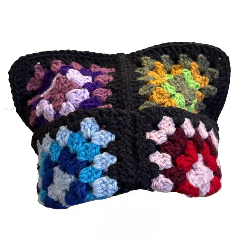 May include: A crochet headband constructed from four square motifs joined by black yarn. Each square features a unique color palette including shades of purple, yellow, green, blue, and red, all framed by a thick black border.