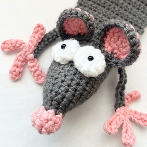 May include: A gray crocheted mouse bookmark with pink ears, nose, and feet. The mouse has large white eyes with black pupils.