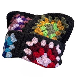 May include: A crochet headband constructed from multiple square motifs joined together. Each square features a black border surrounding a central pattern of yarn in various colors including purple, yellow, green, blue, red, and light pink.