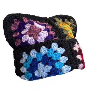 May include: A handmade crochet headband constructed from multiple granny squares. The squares feature vibrant yarn colors including shades of purple, lavender, blue, teal, and yellow, all framed by a thick black yarn border.