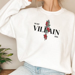 May include: White sweatshirt with a black graphic of a dagger with red roses and the text "IN MY VILLAIN ERA".