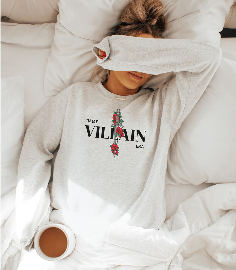 May include: A gray sweatshirt with the text "IN MY VILLAIN ERA" and a black dagger with red roses printed on the front.