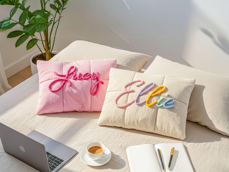 May include: Two decorative throw pillows with personalized names. One pink pillow features the name "Lucy" in a cursive script. The other is off-white with the name "Ellie" in colorful letters. Both pillows have a quilted design.